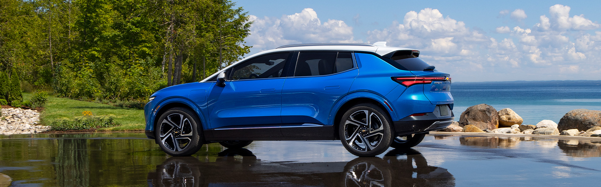 Bright blue Chevrolet Equinox EV with a white roof parked on a wet surface near a body of water.