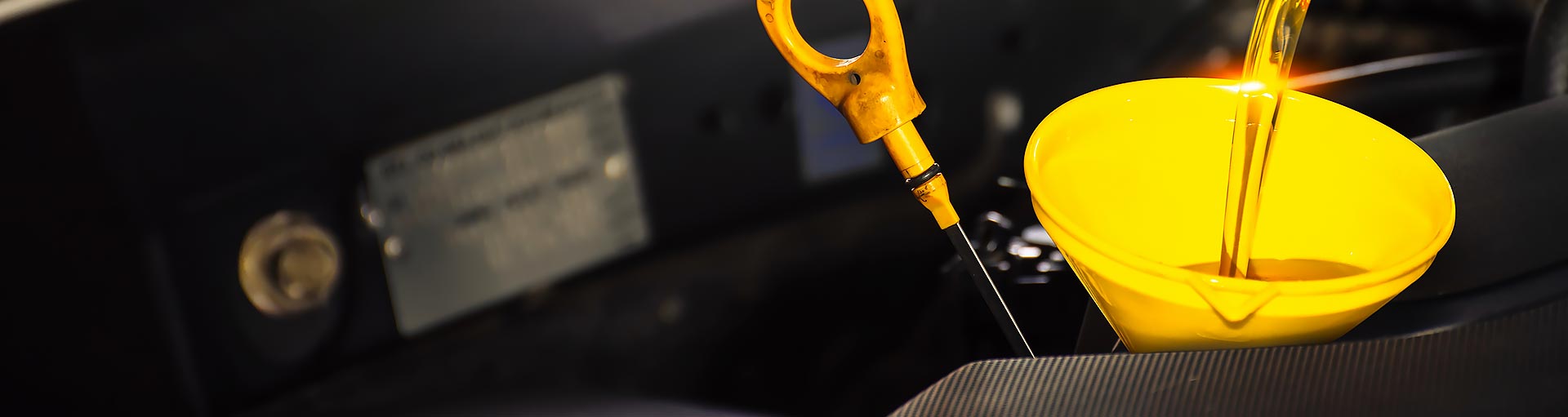 Fresh engine oil being poured into a yellow funnel